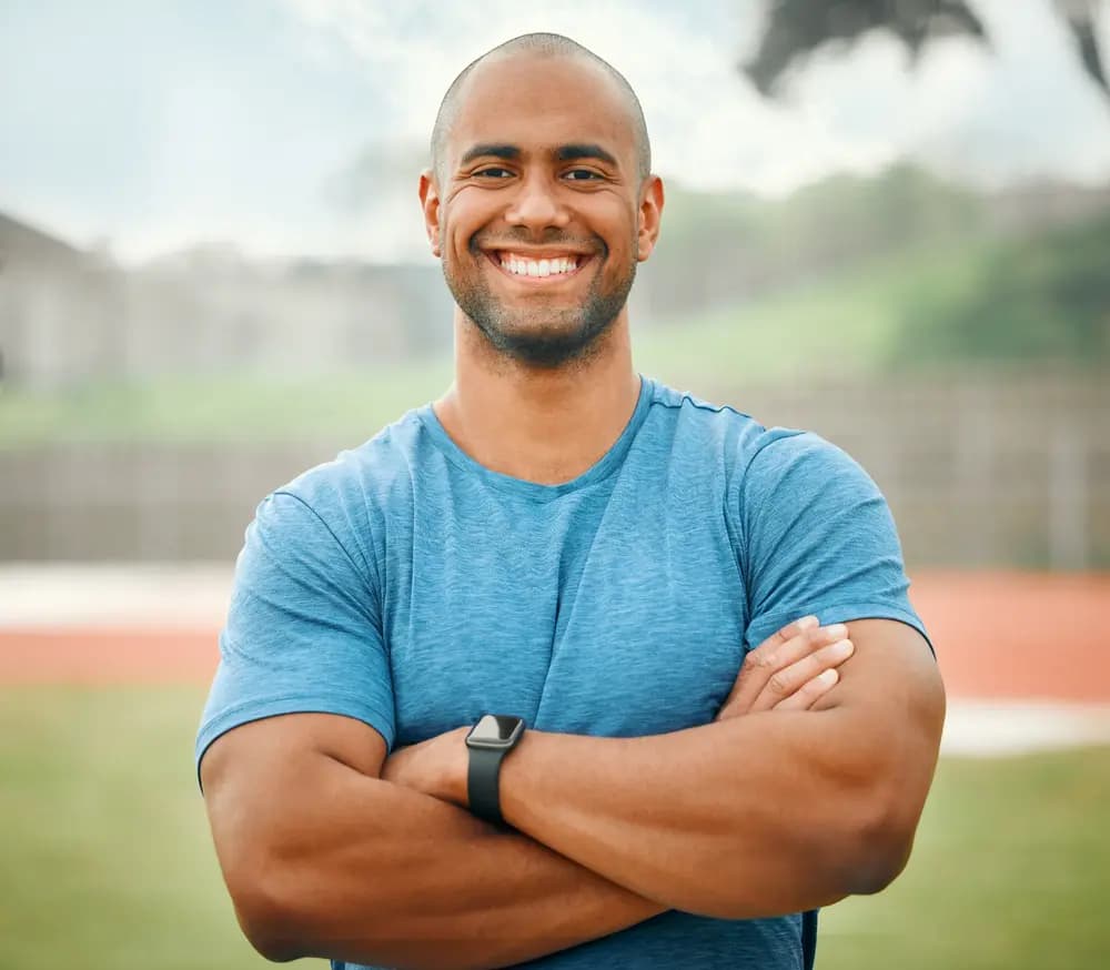 A smiling man standing outdoors in a blue shirt.
